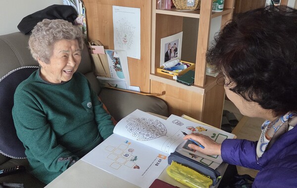 달성군 통합돌봄 서포터즈 '들다봄이' 활동가가 어르신과 함께 인지 워크북을 활용하며 치매 예방 활동을 하고 있다.(사진_달성군)